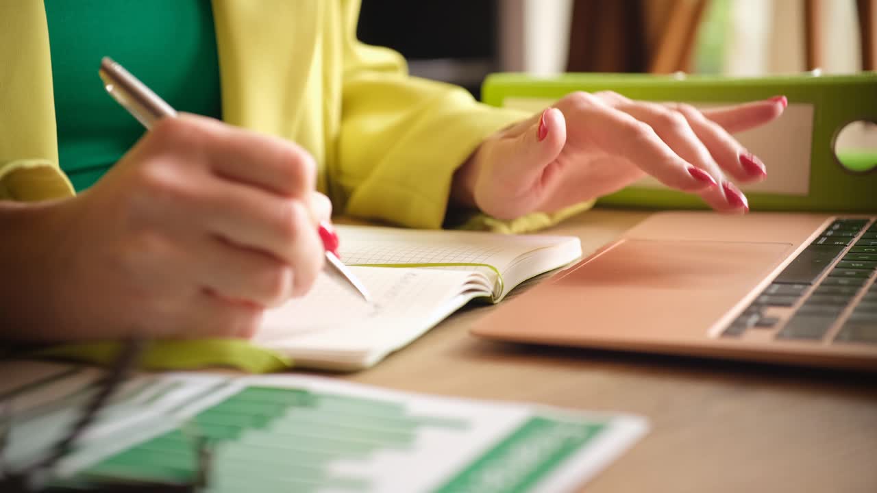 Ragazza scrive con una penna su un quaderno sulla tastiera del computer in ufficio.