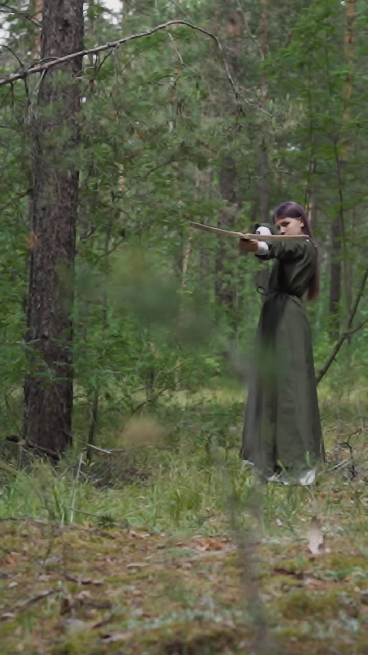 una adolescente con un vestido estilizado dispara una ballesta en una búsqueda en el bosque de pinos verdes. entrenamiento militar de la princesa medieval. uso de armas antiguas en el juego