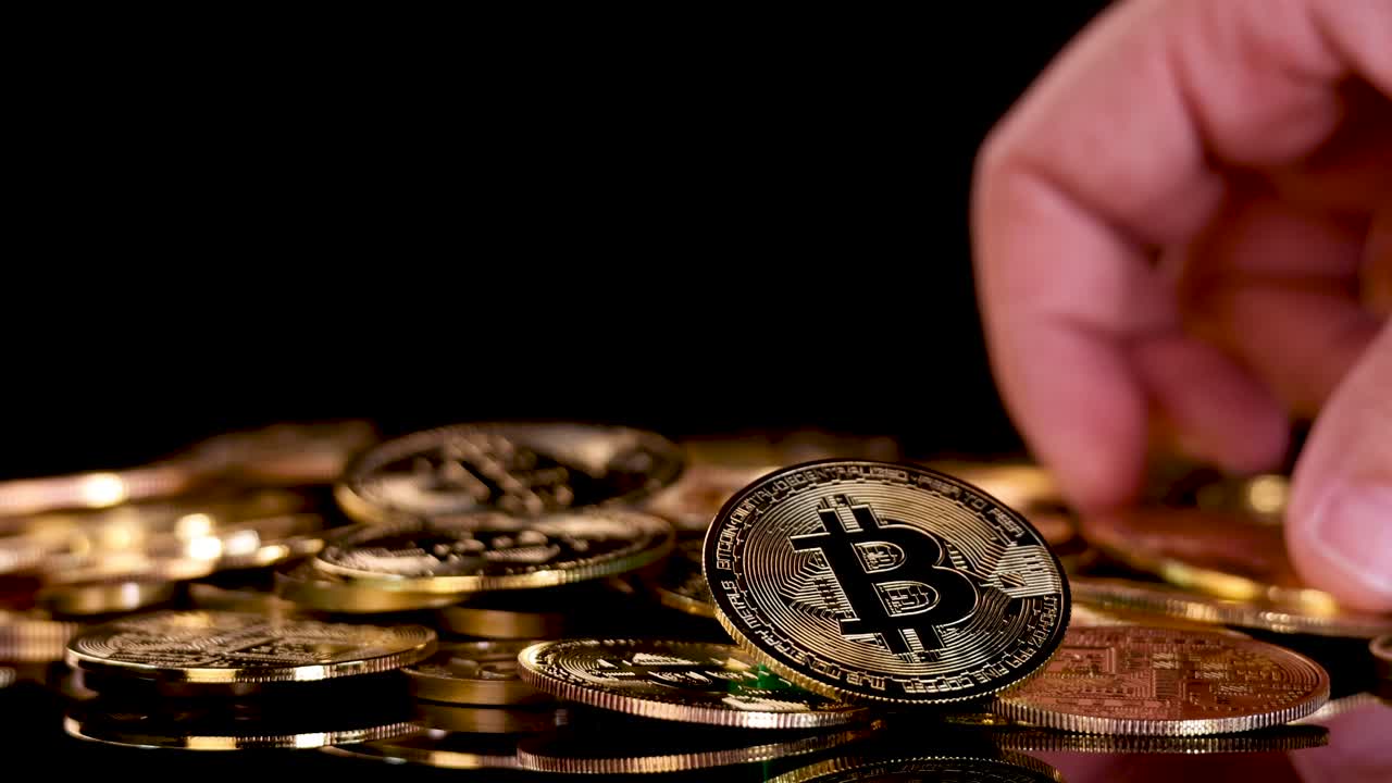 Human hand places gold digital coin onto pile of coins, dramatic lighting, black background