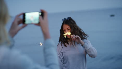 Wunderkerzenfrau-Tanzt-Loop-Mädchen-Mit-Smartphone-Fotografiert-Einen-Freund,-Der-Mit-Wunderkerzen-Am-Strand-Bei-Sonnenuntergang-Tanzt-Und-Silvester-Feiert-Und-Die-Feier-Zum-Unabhängigkeitstag-In-Den-Sozialen-Medien-Teilt