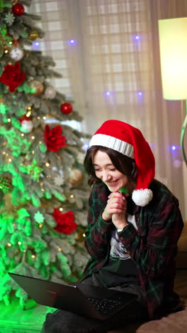 shocked surprised girl in santa cap holds her head in astonishment. success in work online from home. christmas tree at backdrop. vertical video.