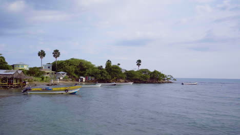 Low-aerial-view-of-Fishermans-Bay-in-Treasure-Beach-Jamaica-with-fishing-boats-floating-on-the-shoreline-and-rising-up-over-the-rocky-outcrop-of-land