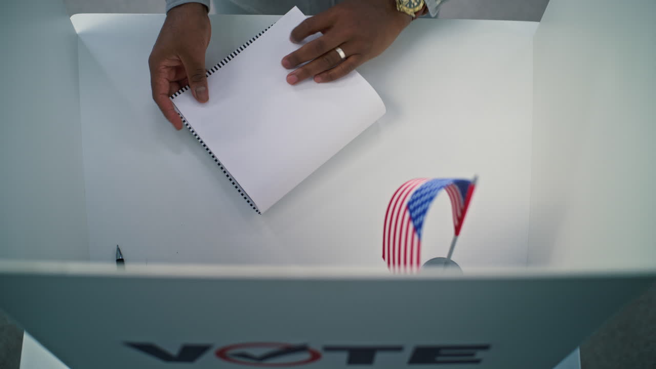 African American us Citizen Filling out Paper Ballot in Voting Booth Close up of Anonymous us Citizen Filling out Paper Ballot in Voting Booth with American Flag African American Man Votes for Presidential Candidates at Polling Station Elections Day in United States