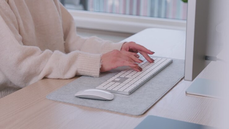 Hände einer Freelancerin, die zu Hause auf einer kabellosen Computertastatur auf dem Tisch tippt.