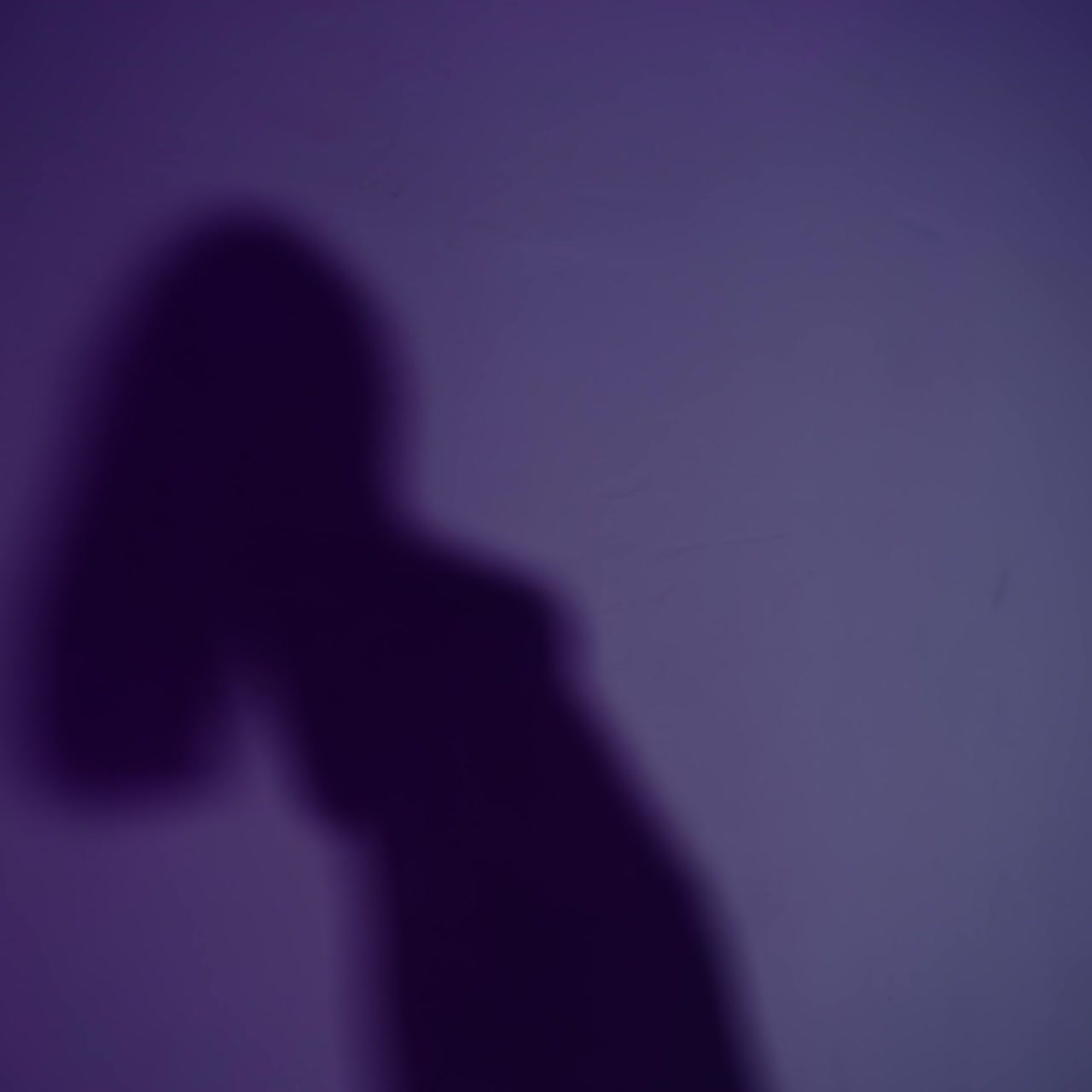 Woman moving in front of the wall lit with purple light. Shadow dancing beautifully