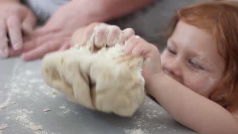 niña sonriente, feliz, preescolar tomando un puñado de harina y agregándola a la masa mientras ayuda en la cocina