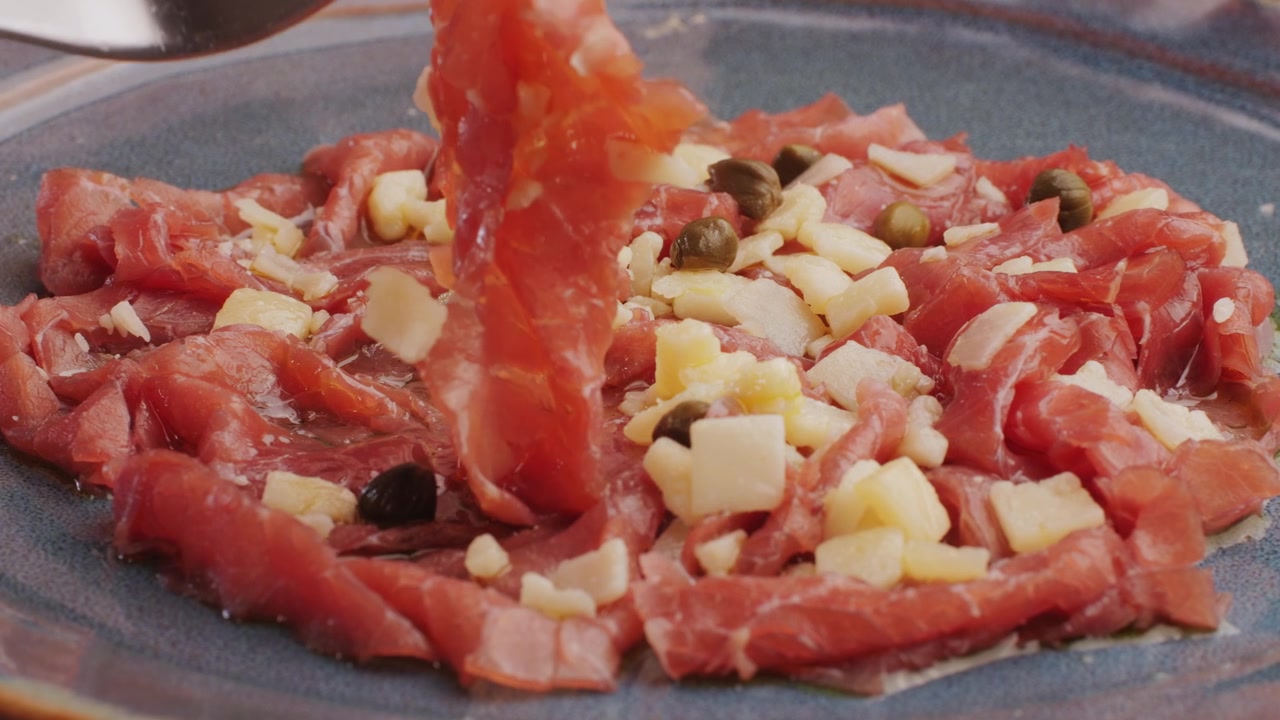 Forchetta che prende una fetta di carpaccio di manzo con formaggio e capperi