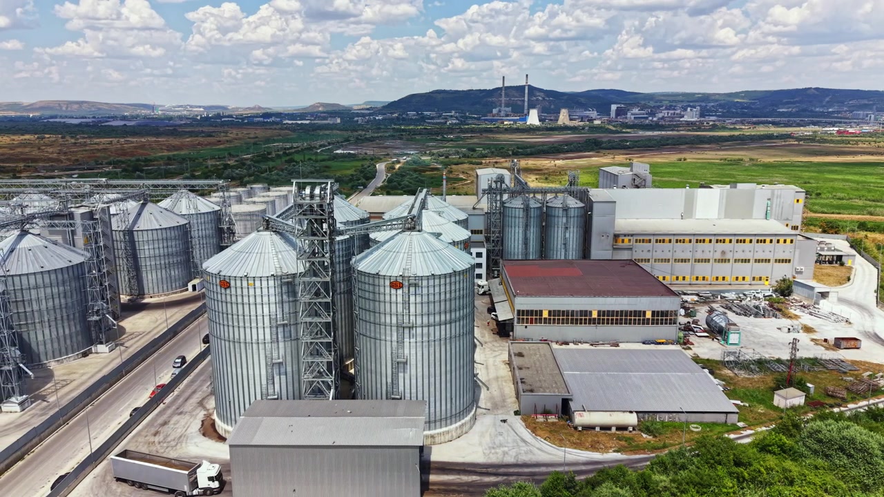 Infrastructure of storage silos and industrial buildings in agriculture area with mountains in background