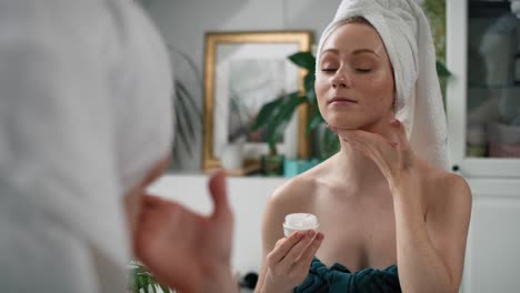 mujer usando crema para la cara después de la ducha en el baño.