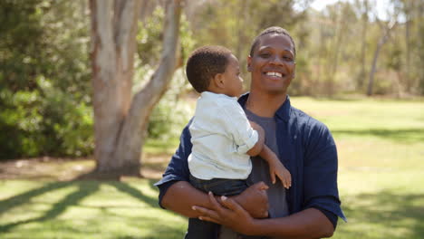 Mixed-race-father-carrying-son-outdoors-walks-into-focus