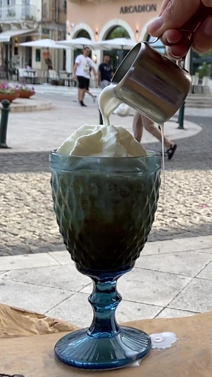 Vertical Slow Motion of Cold Milk Poured Over an Iced Freddo Cappuccino Coffee at an Outdoor Cafe in Corfu, Greece