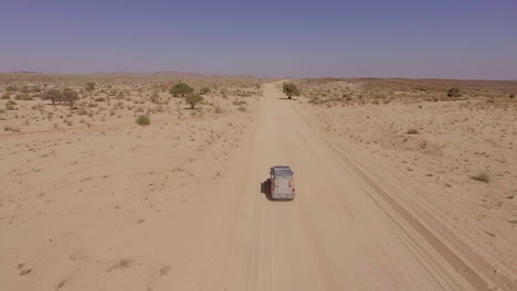 aerial view of off roading truck driving through african desert road, sunny day