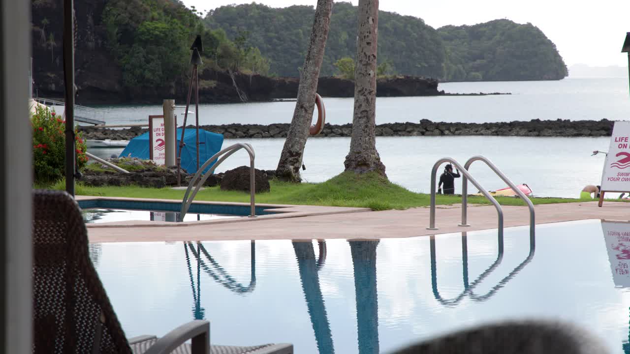 Static wide shot of a luxury resort pool reflecting palm trees against a coastal backdrop