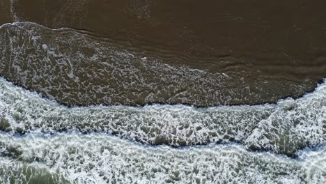 top shot of incoming waves covering whole frame in full width at shallow coast with sand beach