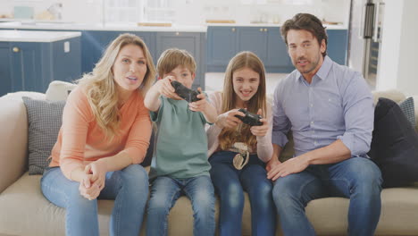 parents having fun sitting on sofa with children at home playing on games console