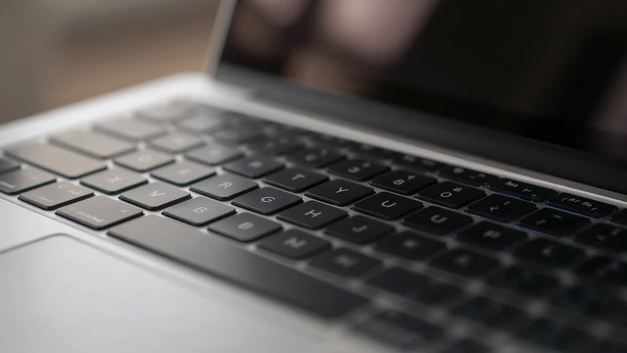 Shifting camera framing laptop keyboard at desk, revealing metal chassis and reflective display