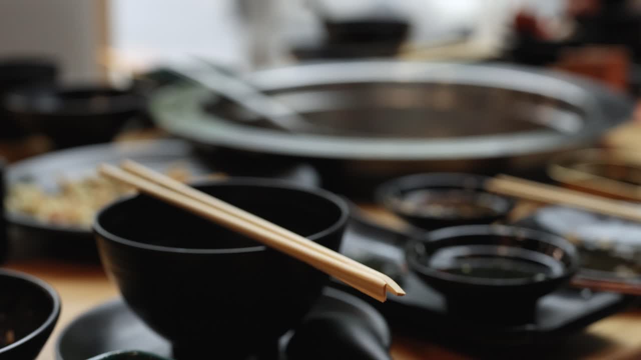 Close-up of chopsticks, black bowls, and hotpot setup with shallow focus and natural lighting