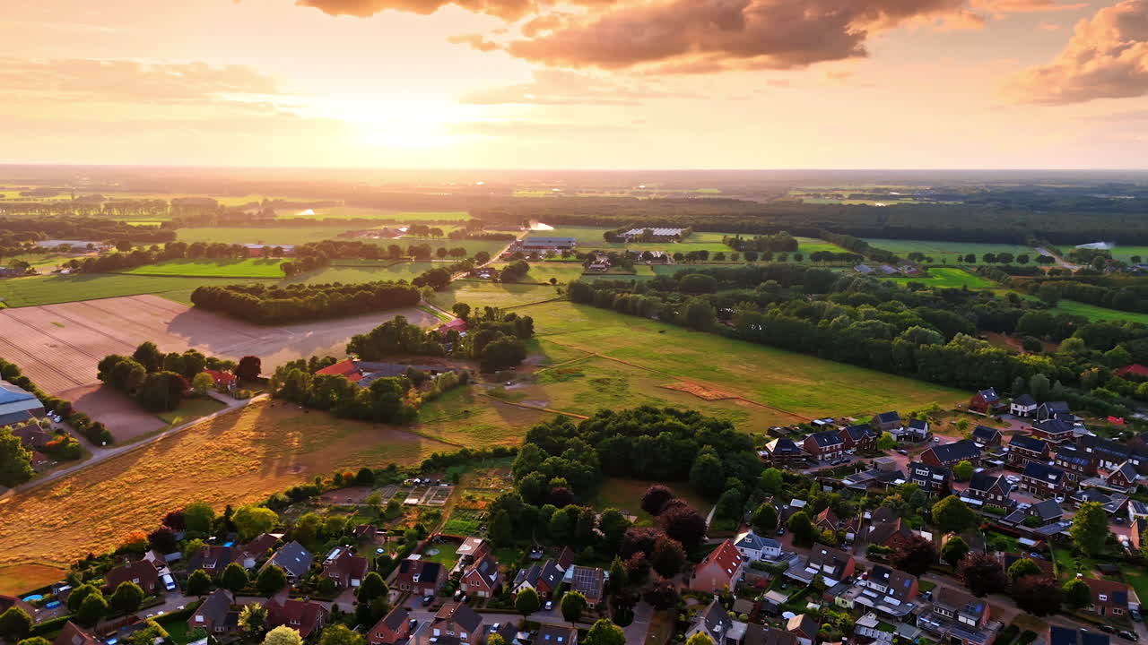 Soft light of setting sun covers the scenery. Drone footage over amazing residential area, fields and forests