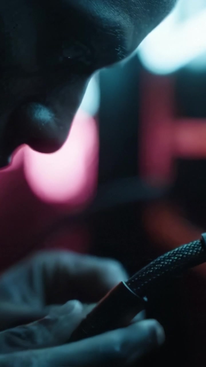 Un primo piano di mani che interagiscono con ingranaggi in un ambiente scarsamente illuminato e intriso di neon, evidenziando l'interazione intima e le dinamiche di connessione della tecnologia.
