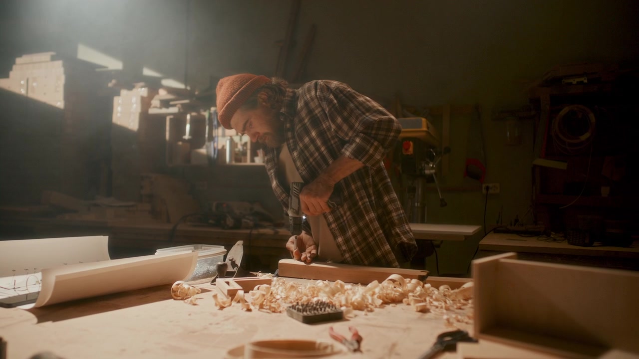 Woodworker Driving Screw into Wooden Piece with Electric Drill in Workshop