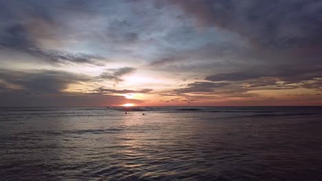 Drone-shot-pushing-in-on-waves-and-surfers-in-Aruba,-Caribbean-with-spectacular-sunset