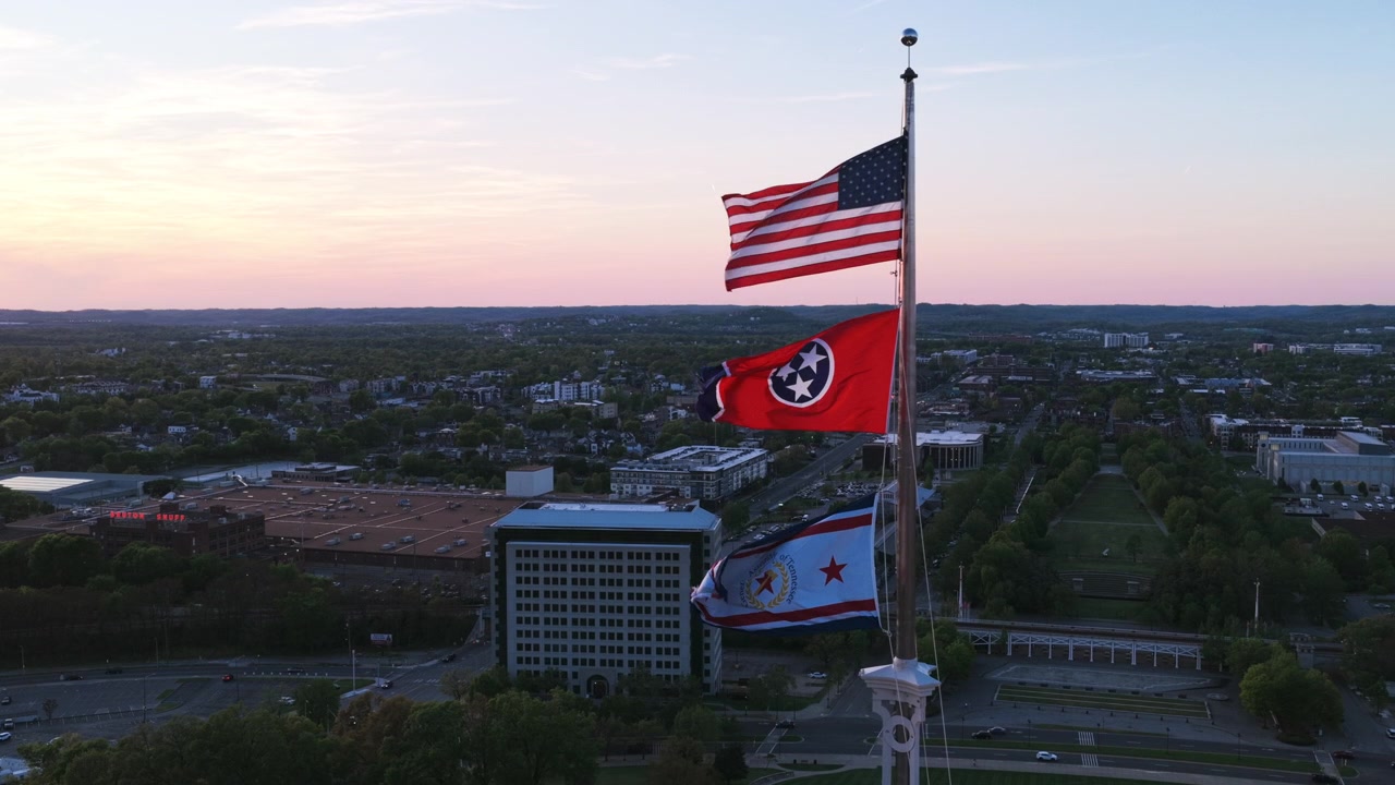 Vista aerea con drone delle bandiere degli Stati Uniti, dello stato del Tennessee e della città di Nashville che sventolano in cima alla cupola del Campidoglio dello Stato del Tennessee al tramonto sul paesaggio urbano circostante