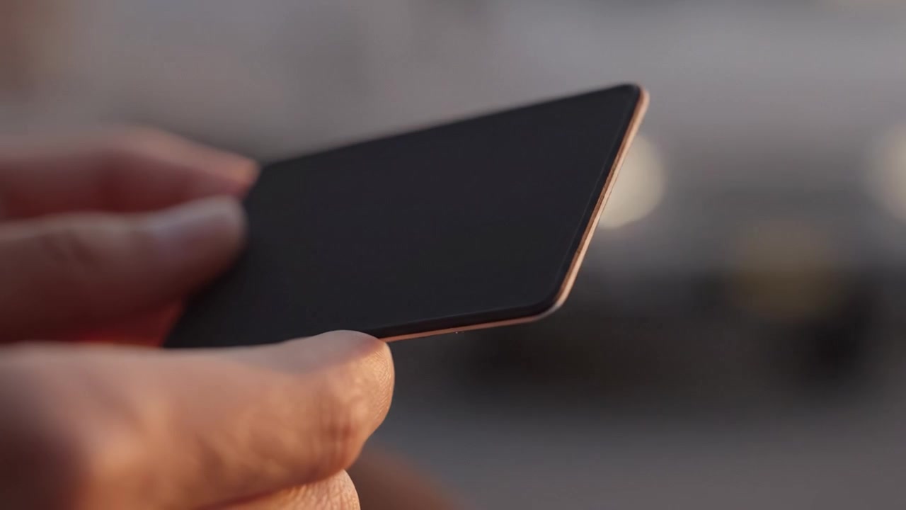 Una vista ravvicinata di una mano che tiene una carta elegante e minimalista sotto il tenue bagliore della luce naturale, mettendo in mostra design moderno e dettagli