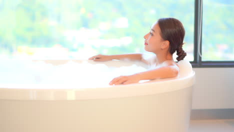 side view of sexy asian girl lying inside a bathtub with foam at home