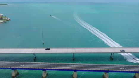 Luftaufnahme-Der-Verfolgung-Von-Autos-über-Die-Seven-Mile-Bridge-In-Den-Florida-Keys,-Während-Ein-Boot-Darunter-Vorbeifährt