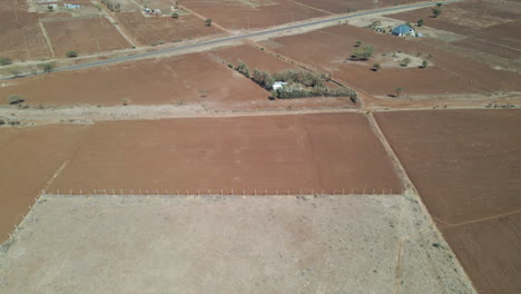 inclinación aérea de un paisaje árido en la zona rural de kenia que revela un pequeño pueblo en la distancia