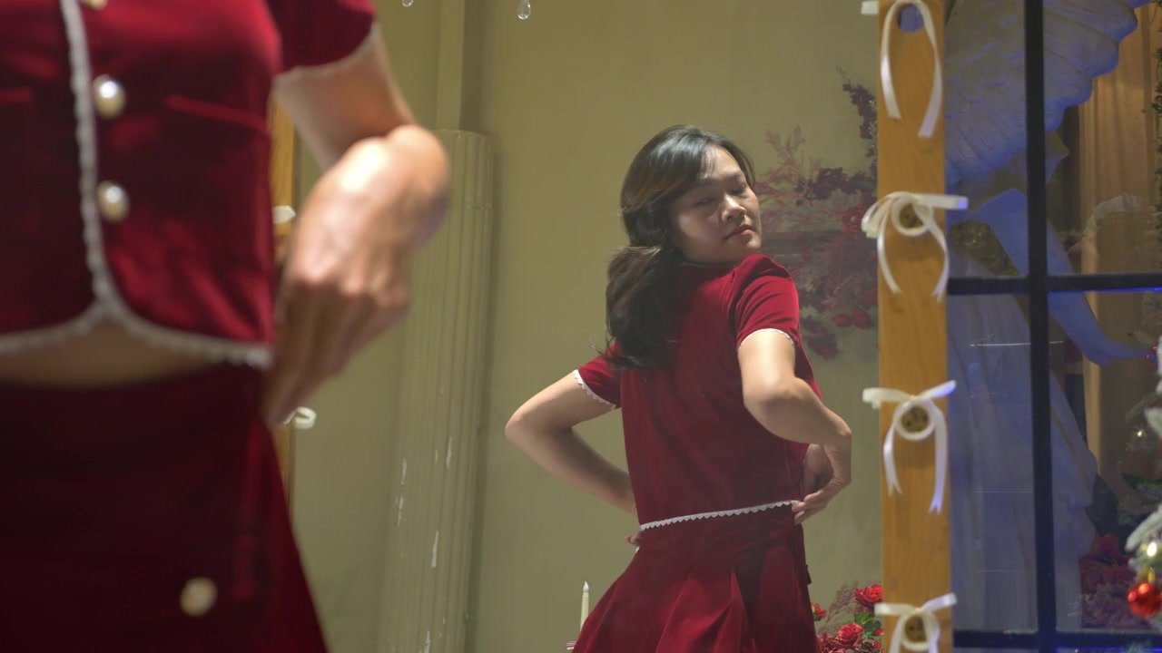 Donna asiatica in un elegante abito rosso aderente mentre si guarda allo specchio.