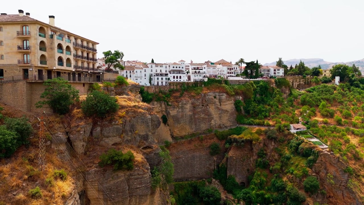 Panorering hen over Rondas klippeside med Parador de Ronda og hvide huse over frodig vegetation, marker og dramatisk landskab nedenfor