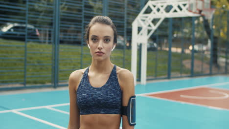 retrato de una mujer deportiva con airpods sonriendo alegremente a la cámara mientras está de pie en la cancha deportiva en un día de verano