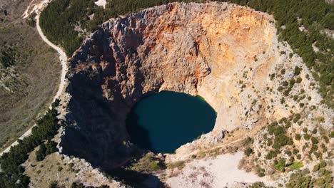 an aerial shot of red lake or crveno jezero which is a collapsed sinkhole containing a karst lake close to imotski, croatia