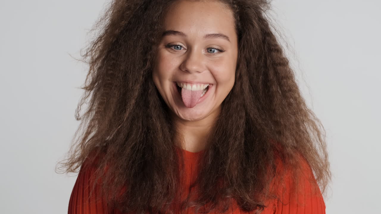 una mujer caucásica de cabello rizado haciendo caras divertidas ante la cámara.