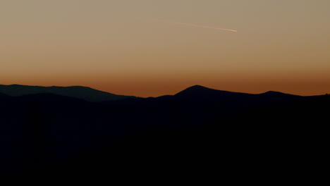 Silhouetted-mountain-horizon-with-plane-flying