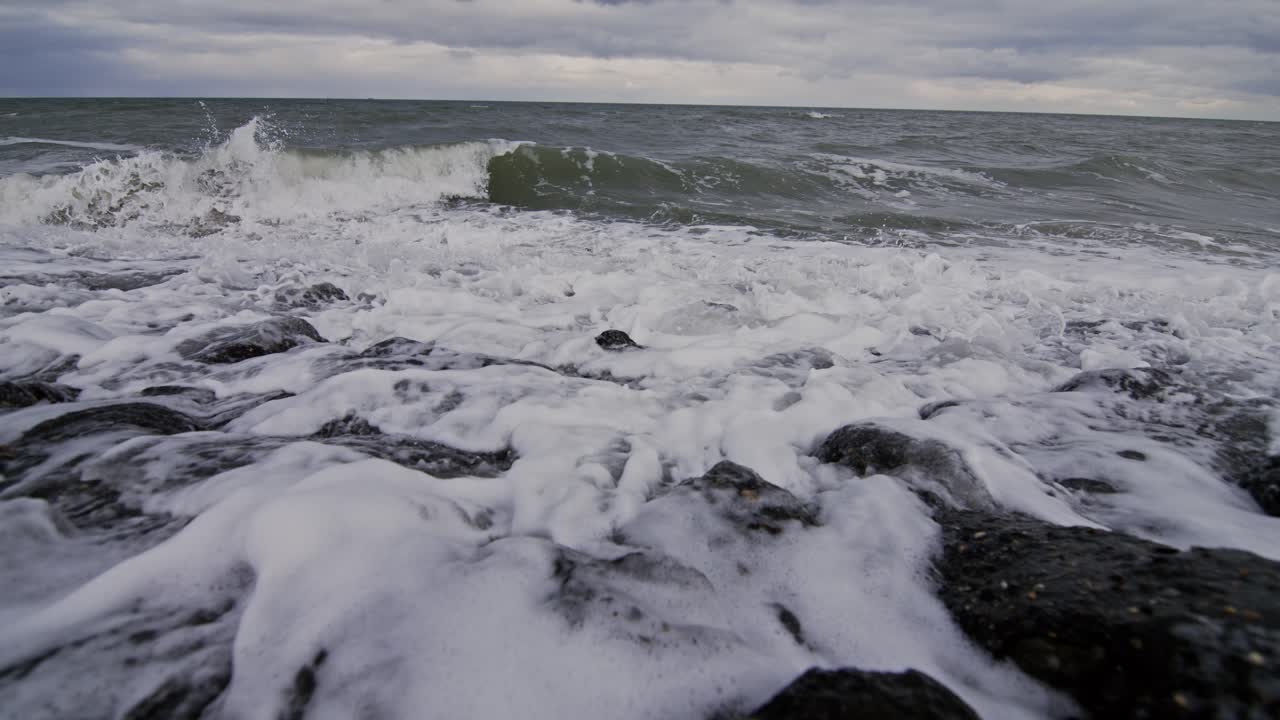 Waves crashing over rocks, foam splashing on a beach in Domburg, The Netherlands, super slow motion