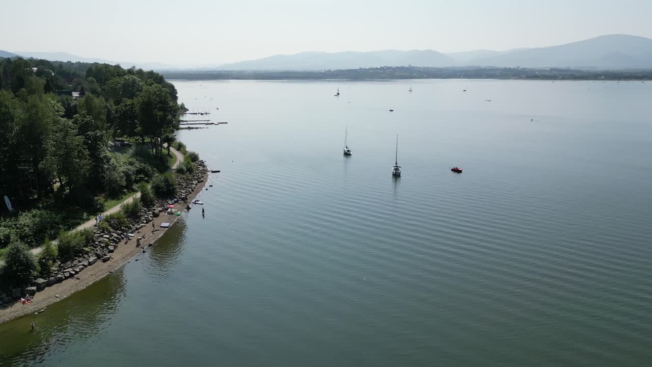línea de costa de un tranquilo lago de montaña en las montañas beskid, rodeado de vegetación durante un día de verano - vista aérea 4k