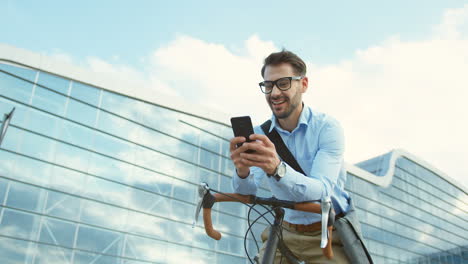 hombre de negocios feliz sentado en una bicicleta y escribiendo en su teléfono inteligente en el centro de la ciudad