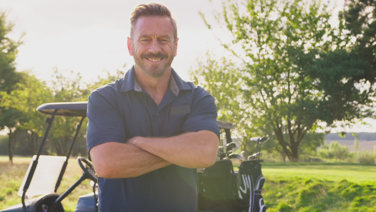 Portræt af smilende moden mandlig golfspiller, der står ved en golfvogn på golfbanen