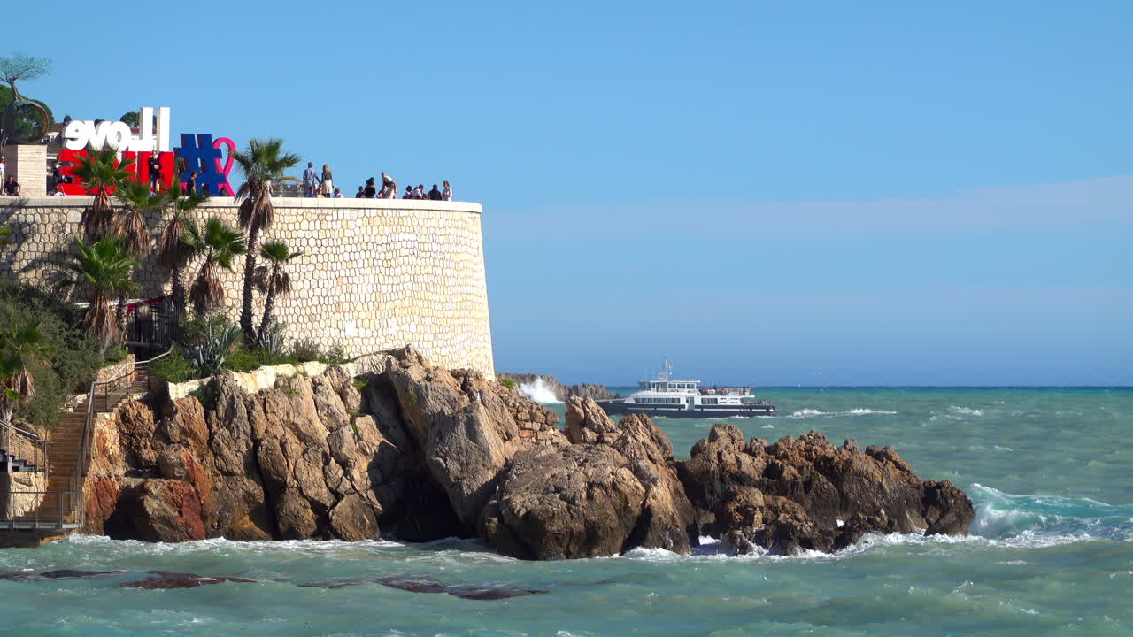 Nice, France - July 3, 2025: View of the I Love Nice sign on the Promenade des Anglais, with tourists enjoying the lookout and a passenger boat cruising across the Mediterranean Sea