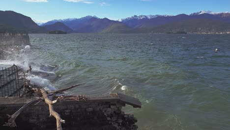 waves crashing of maggiore lake shore with alps mountain range in background, stresa in italy