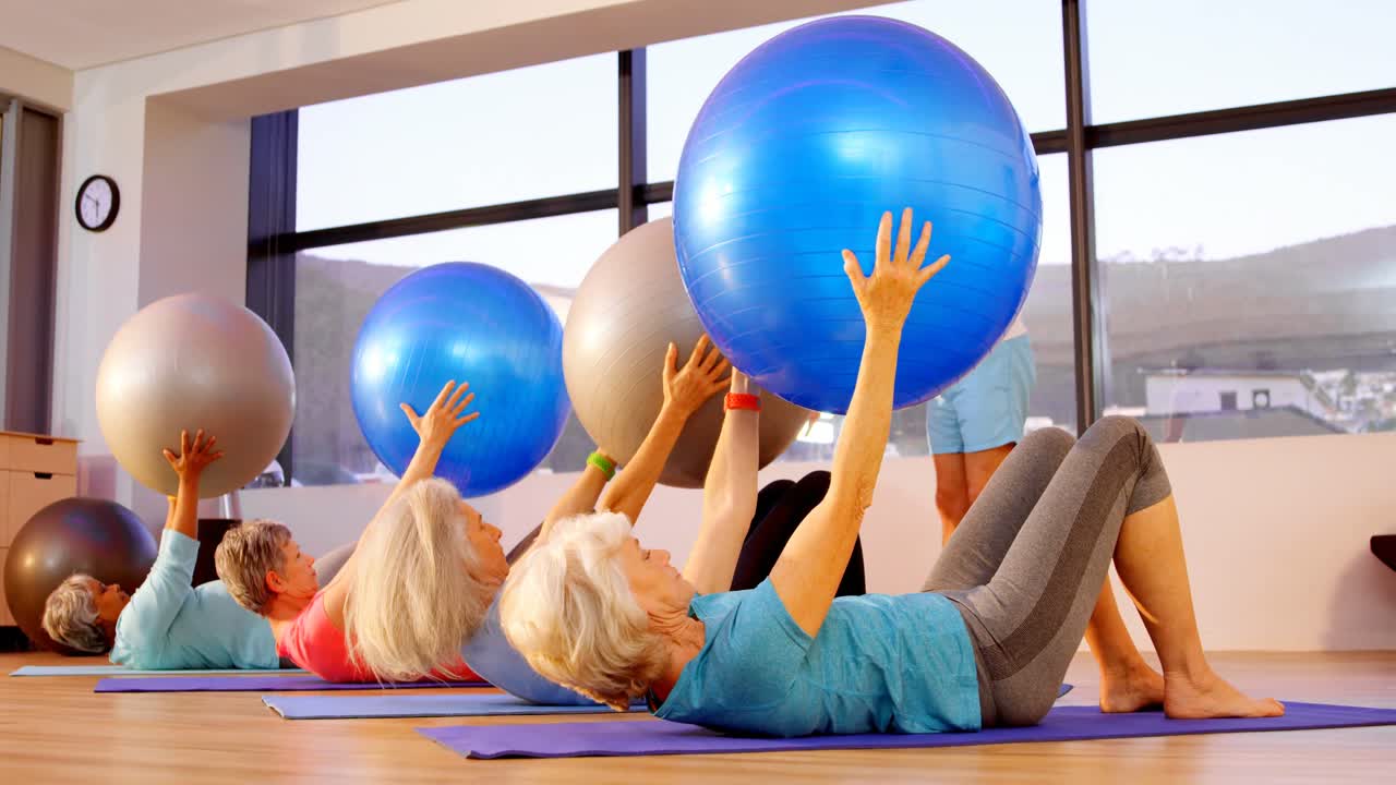 Trainer assisting senior woman in performing yoga 4k