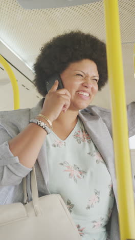 vertical video of happy plus size biracial woman using smartphone in bus
