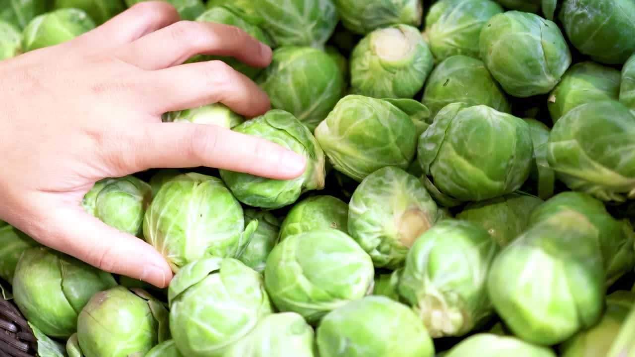 A hand carefully picks through a pile of fresh Brussels sprouts, highlighting the selection process.