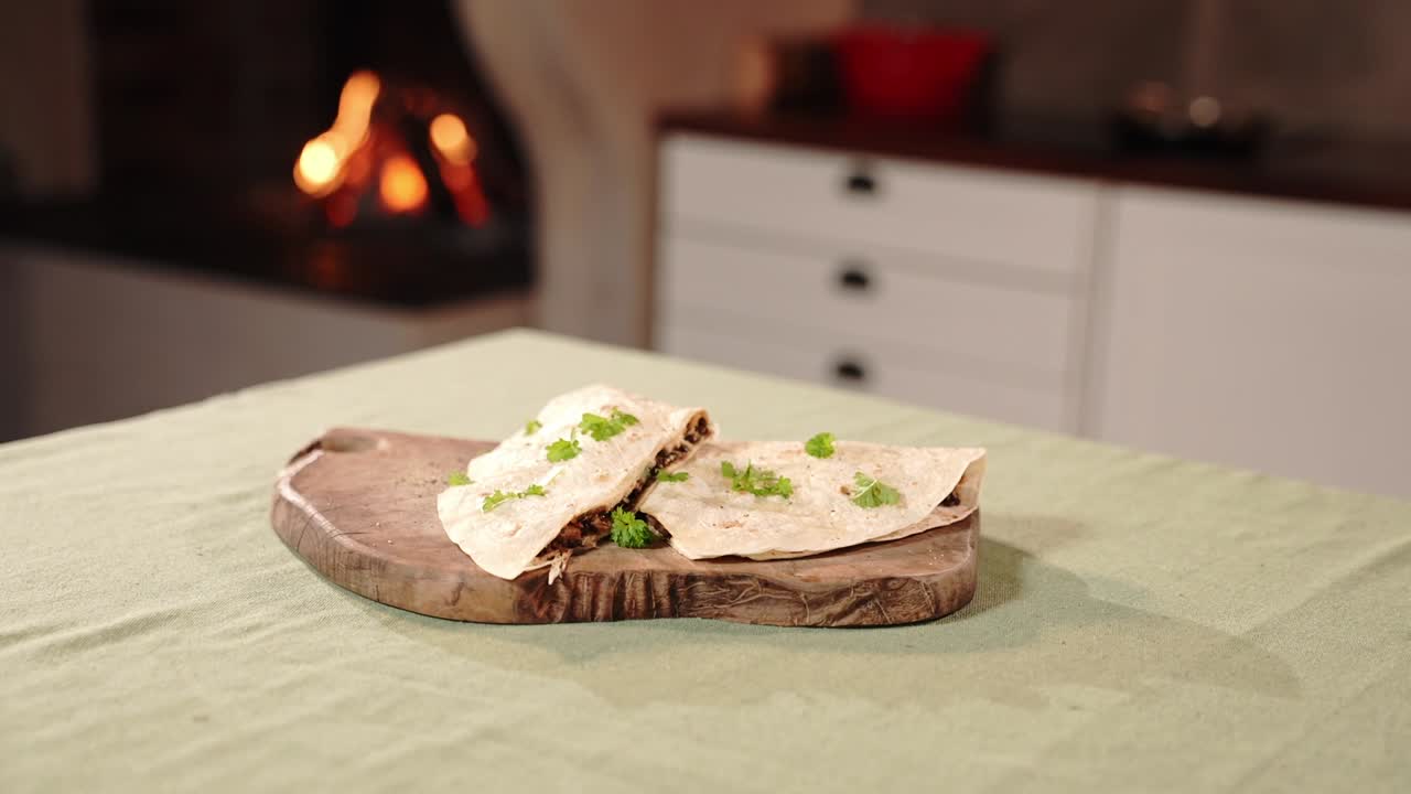 Video ravvicinato di pane rustico servito con crema spalmabile ed erbe aromatiche su un tagliere di legno. Atmosfera accogliente di cucina domestica con camino, luce calda e presentazione tradizionale del cibo