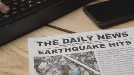 Newspaper-Headline-Featuring-Devastation-Caused-By-Earthquake-Disaster-On-Desk-Next-To-Computer-Keyboard-And-Phone