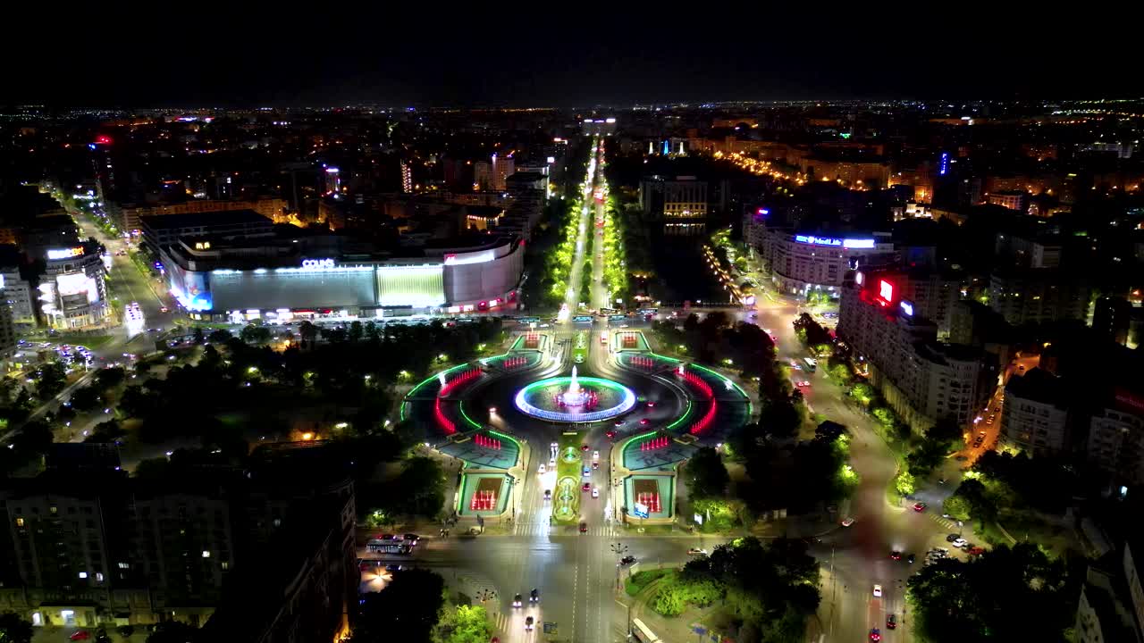 Top view of city center of Bucharest at night. Night traffic. The famous artesian fountains colored in different shades. Unirea Shopping Center on the left. Travel destination and capital of Romania
