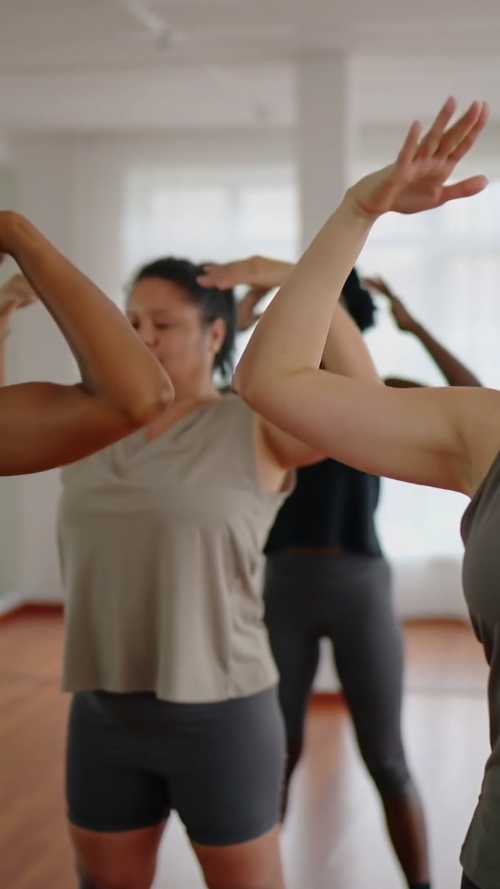 Vertical video: After cue woman doing arm mobility for warmup in studio in gray top, watch visible