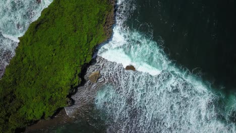 overhead view of huge coral rock with clusters of small rocks hits by the wave on the beach with